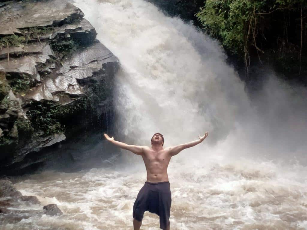 A man standing in front of a waterfall with his arms outstretched, captured in an image gallery.