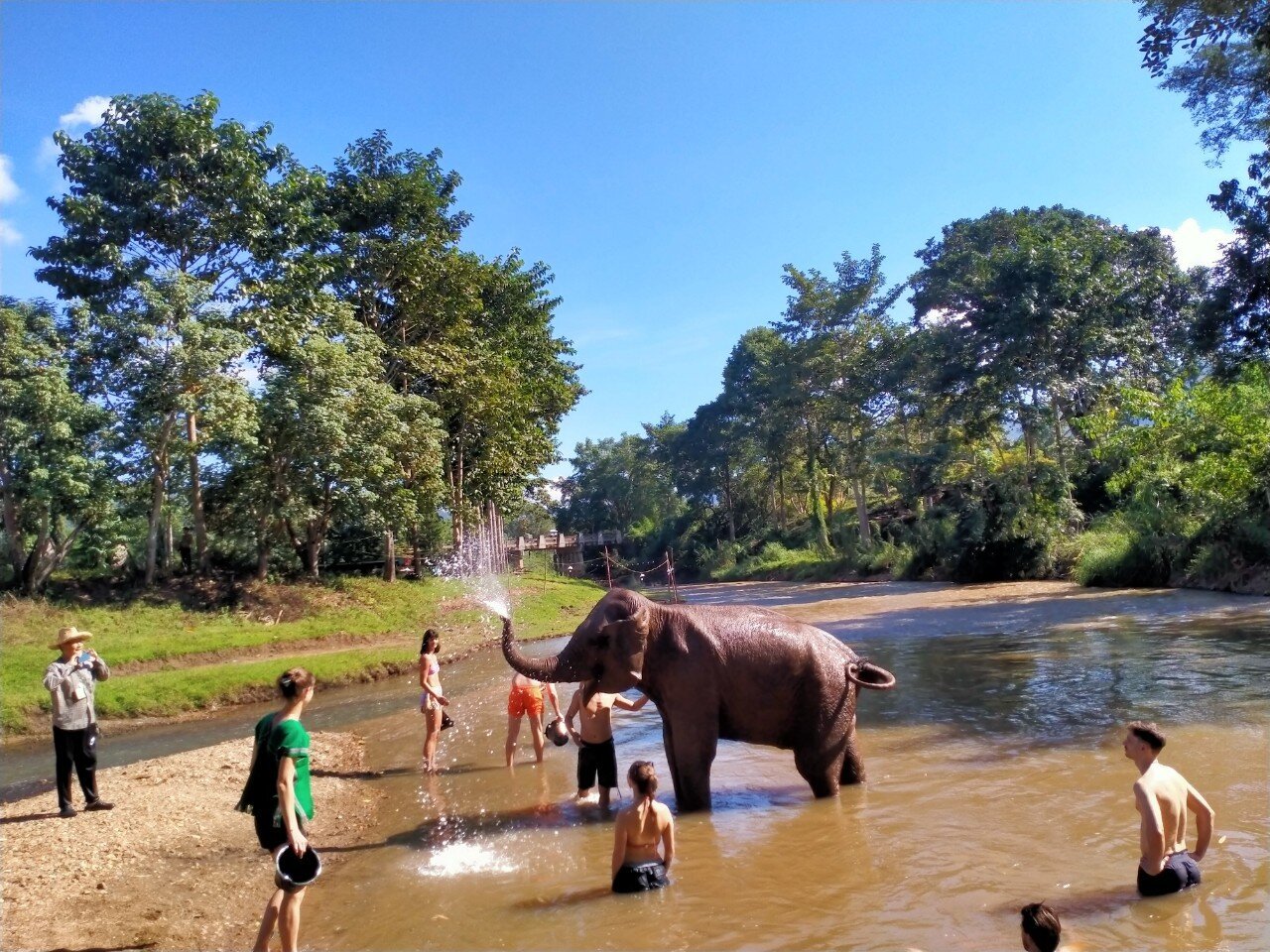 A group of people enjoying the company of an elephant in a river.