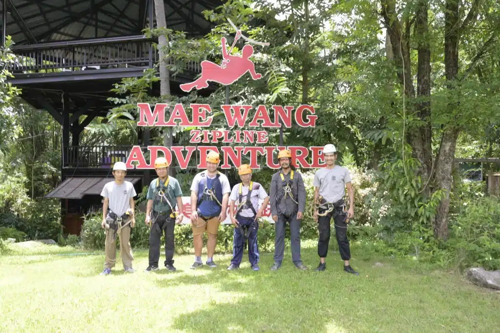 A group of people standing in front of a sign that says mae wang adventure, ready for their ziplining chiang mai experience.